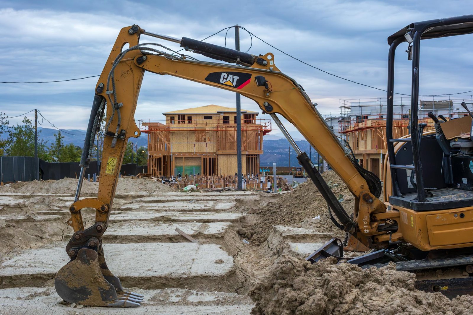 Excavator working on a new residential construction site with wooden frames.